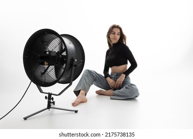 A Beautiful Young Woman Is Sitting In A Bright Room On The Floor Cooling Down Under A Fan