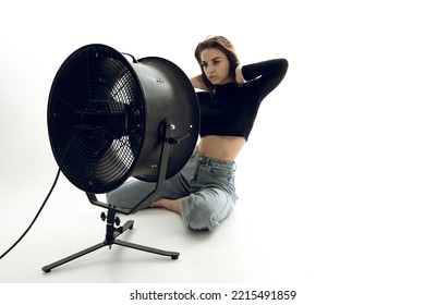 A Beautiful Young Woman Is Sitting In A Bright Room On The Floor Cooling Down Under A Fan	
