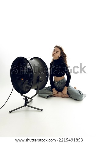 a beautiful young woman is sitting in a bright room on the floor cooling down under a fan	
