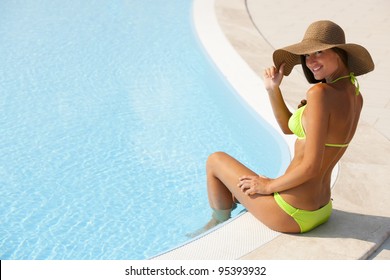 Beautiful young woman sitting by swimming-pool
