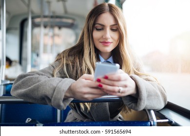 Beautiful Young Woman Sitting In City Bus And Typing A Message On The Phone. 