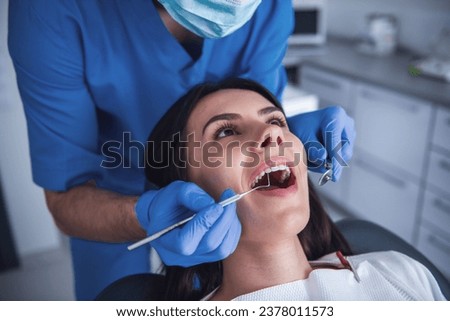 Beautiful young woman is sitting in dentist's chair while doctor is examining her teeth