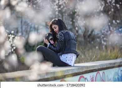 Beautiful Young Woman Sitting With Her Black Dog In An Abandoned Pool Among Cherry Blossoms