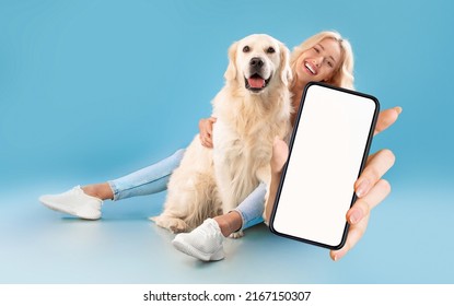 Beautiful young woman sitting with her dog and showing big blank smartphone with white screen at camera, happy pet owner recommending new mobile app or website while posing on blue background, mockup - Powered by Shutterstock