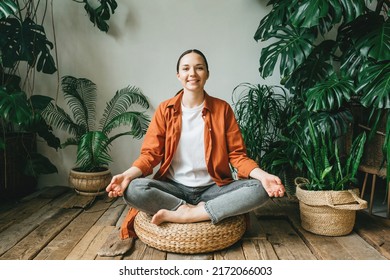 A beautiful young woman is sitting in meditation in the lotus position in a beautiful green garden among the plants of the house. The concept of mindfulness, psychological and mental health. - Powered by Shutterstock