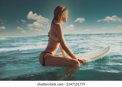 Beautiful young woman sitting on her surfboard waiting for the waves - Powered by Shutterstock