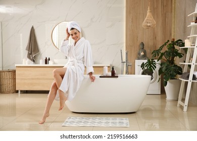 Beautiful young woman sitting on edge of tub in bathroom