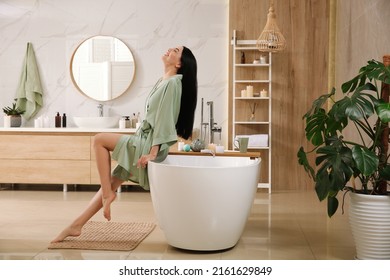 Beautiful young woman sitting on edge of tub in bathroom - Powered by Shutterstock