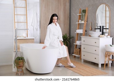 Beautiful young woman sitting on edge of tub in bathroom - Powered by Shutterstock