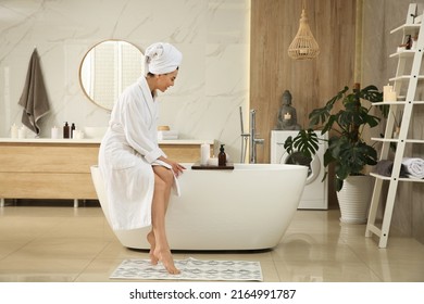 Beautiful Young Woman Sitting On Edge Of Tub In Bathroom