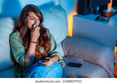 Beautiful young woman sitting on couch late at night, sad while watching drama movie on TV, crying and wiping tears with paper tissues - Powered by Shutterstock