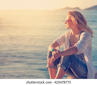 beautiful young woman sitting on the beach and watching the sunset