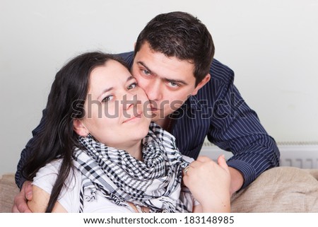 Beautiful young woman sitting on couch and her husband nearby