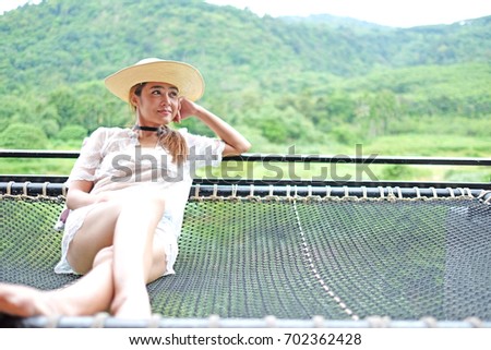 Beautiful young woman sitting on the net at mountain background. Her have beauty hat for fashion summer,She look like very happy very much.