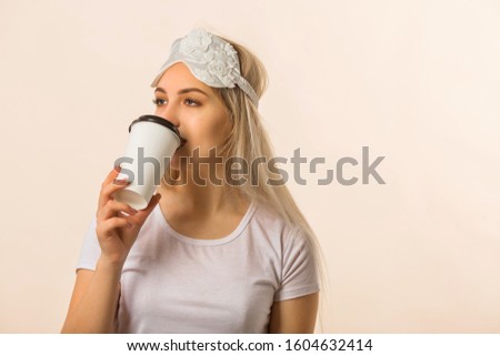 beautiful young woman in a sleep mask drinks coffee on a beige background