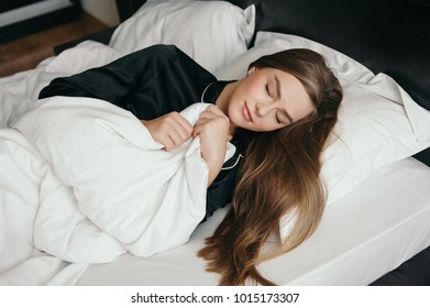 Beautiful young woman sleeping in bed covered by blanket on white linen clothed eyes and smiling