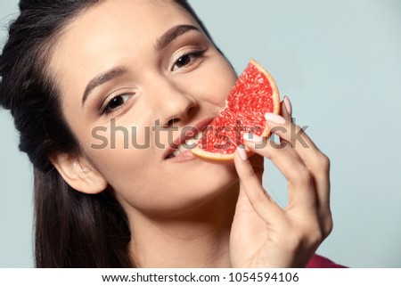 Beautiful young woman with slice of citrus fruit on color background, closeup
