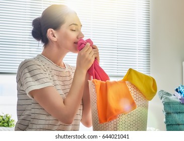 Beautiful Young Woman Is Smelling Clean Clothes And Smiling While Doing Laundry At Home.