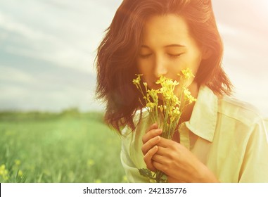 Beautiful Young Woman Smelling Yellow Flowers With Closed Eyes In Summer Outdoor. Image With Sunlight Effect