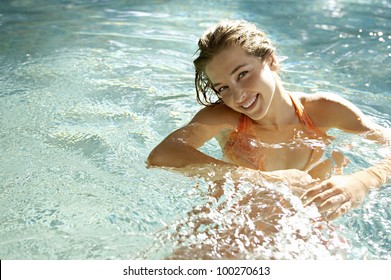 Beautiful young woman smiling in a swimming pool, under the golden summer light.