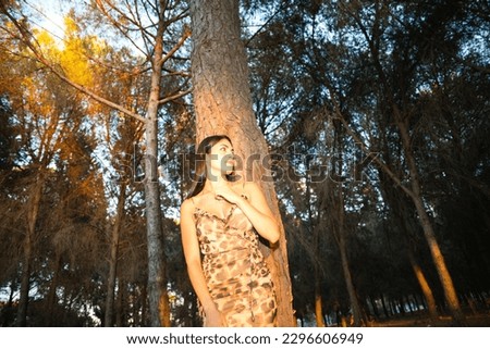 beautiful young woman from south america leaning on a tree in the forest in the golden hour. Rays of sunlight enter through the trees in autumn and create golden atmosphere.