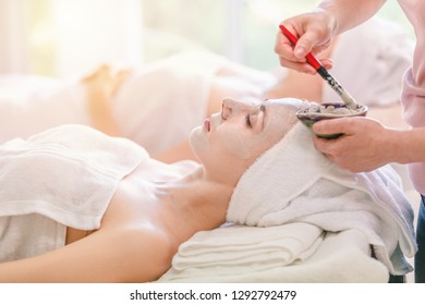 Beautiful young woman spa applying cosmetic mask cream on face relaxing receiving massage,Spa face concept