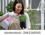 Beautiful young woman spends her weekends tending to the plants in her garden, spraying beautiful flowering plants with water sprayer at home