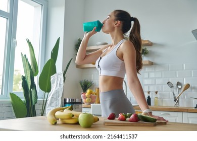 Beautiful young woman in sports clothing drinking protein cocktail while standing at the kitchen - Shutterstock ID 2164411537