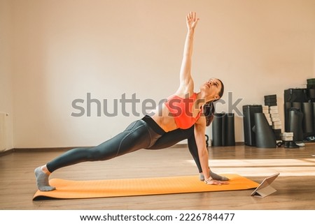 Beautiful young woman in sportswear doing stretching while yoga pose on the floor in front of window at gym. 