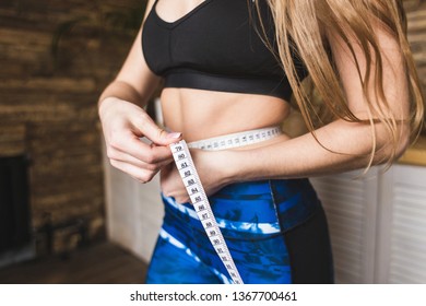 Beautiful young woman in sportswear measures the measured flight waist circumference. Sport, diet and weight loss