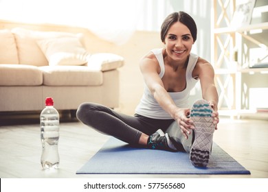 Beautiful young woman in sportswear is smiling while stretching on yoga mat at home