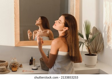 A beautiful young woman sprays perfume on her neck while standing in the bathroom. - Shutterstock ID 2133853253