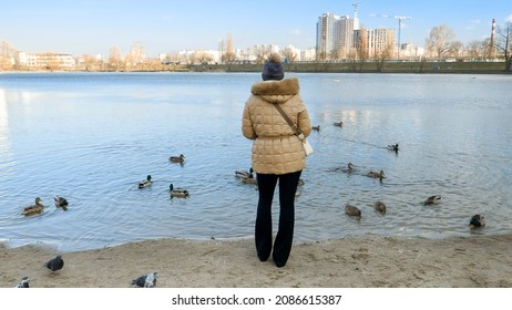 Beautiful Young Woman Standing At The Lake And Feeding Ducks And Birds With Bread