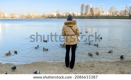 Beautiful young woman standing at the lake and feeding ducks and birds with bread