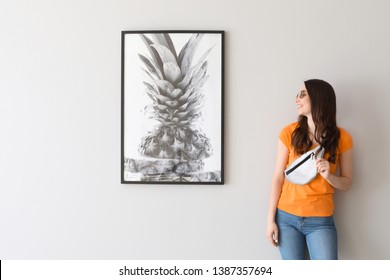 Beautiful Young Woman Standing Near Picture Hanging On Light Wall