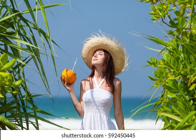 beautiful young woman standing on the sand beach and holding a coconut drink