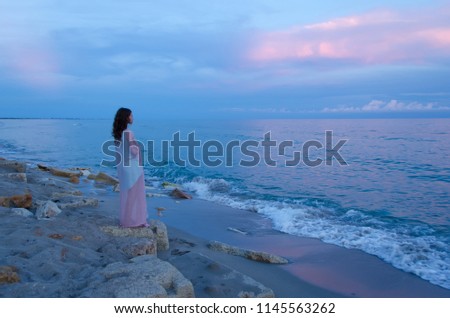 Beautiful young woman standing on the beach at sunset.