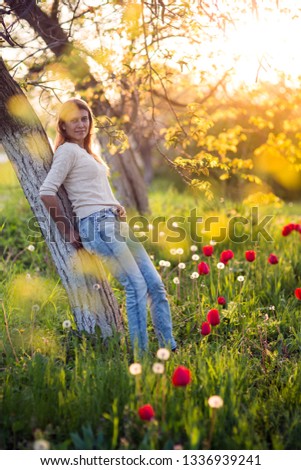 Beautiful young woman  standing on a clearing of green grass with blooming tulips at sunset