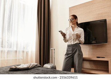 Beautiful young woman stands in a modern bedroom, sipping coffee and looking at her phone. - Powered by Shutterstock