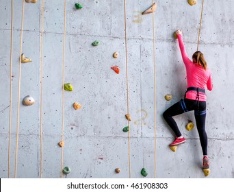 Beautiful young woman starts to climbing big artificial wall