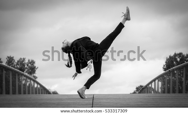 Beautiful young woman in a strict black and\
white jacket doing contemporary jazz dance moves on a wooden bridge\
in a modern business\
district
