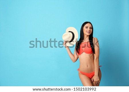 Beautiful young woman in stylish bikini with hat on light blue background. Space for text