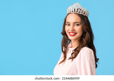 Beautiful young woman in stylish dress and tiara on blue background