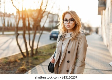 Beautiful Young Woman In Stylish Glasses And Trendy Coat With Handbag In The Day Of Spring At Sunset