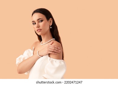 Beautiful young woman with stylish pearl jewelry on beige background