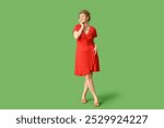 Beautiful young woman in stylish red dress on green background