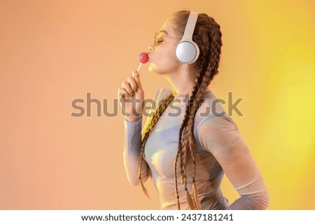 Beautiful young woman with stylish sunglasses and lollipop listening music on color background