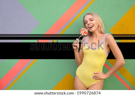 Beautiful young woman in stylish swimsuit and with lollipop on color background