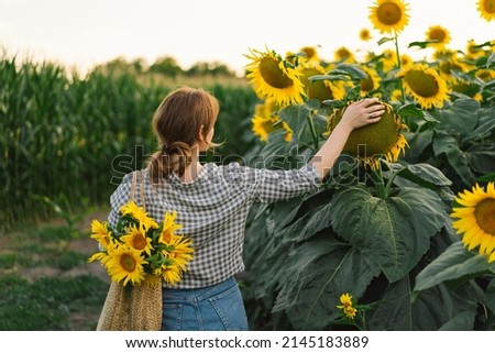 Beautiful young woman with sunflowers enjoying nature and laughing on summer sunflower field. Woman holding sunflowers. Sunflare, sunbeams, glow sun, freedom and happiness concept.
