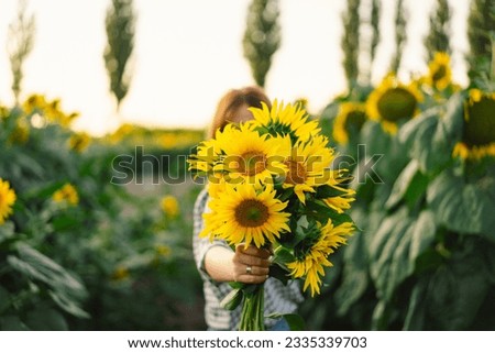 Beautiful young woman with sunflowers enjoying nature and laughing on summer sunflower field. Woman holding sunflowers. Sunflare, sunbeams, glow sun, freedom and happiness concept.